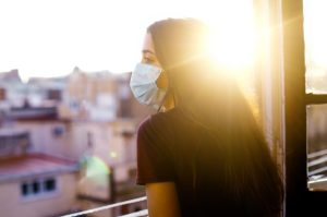 mujer con mascarilla mirando desde una ventana